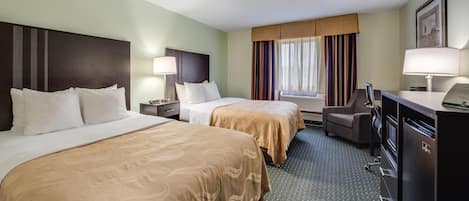 A hotel room with two beds, a desk, a chair, a refrigerator, and a window with curtains.