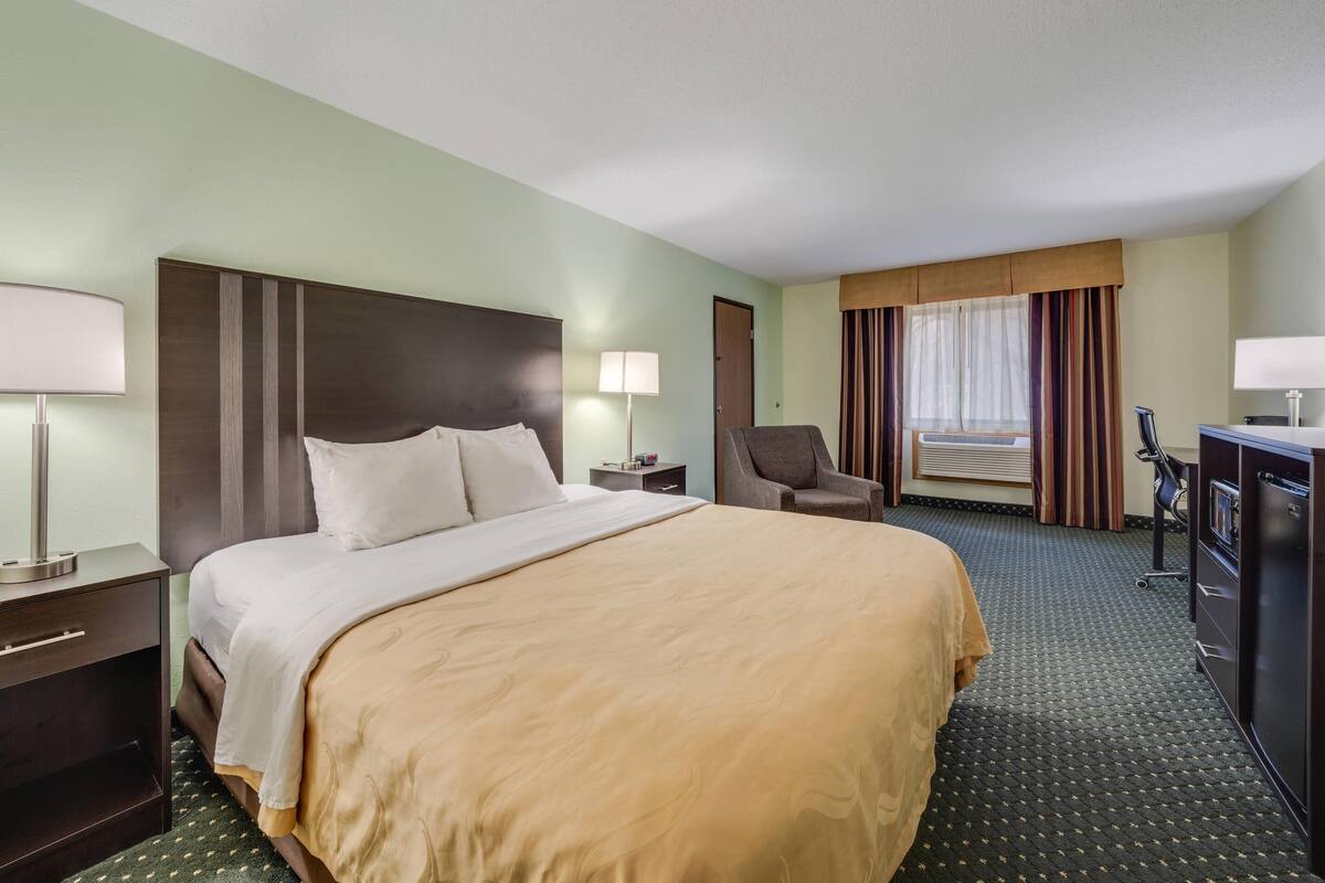 A hotel room with a large bed, a desk, a chair, and a window with curtains.