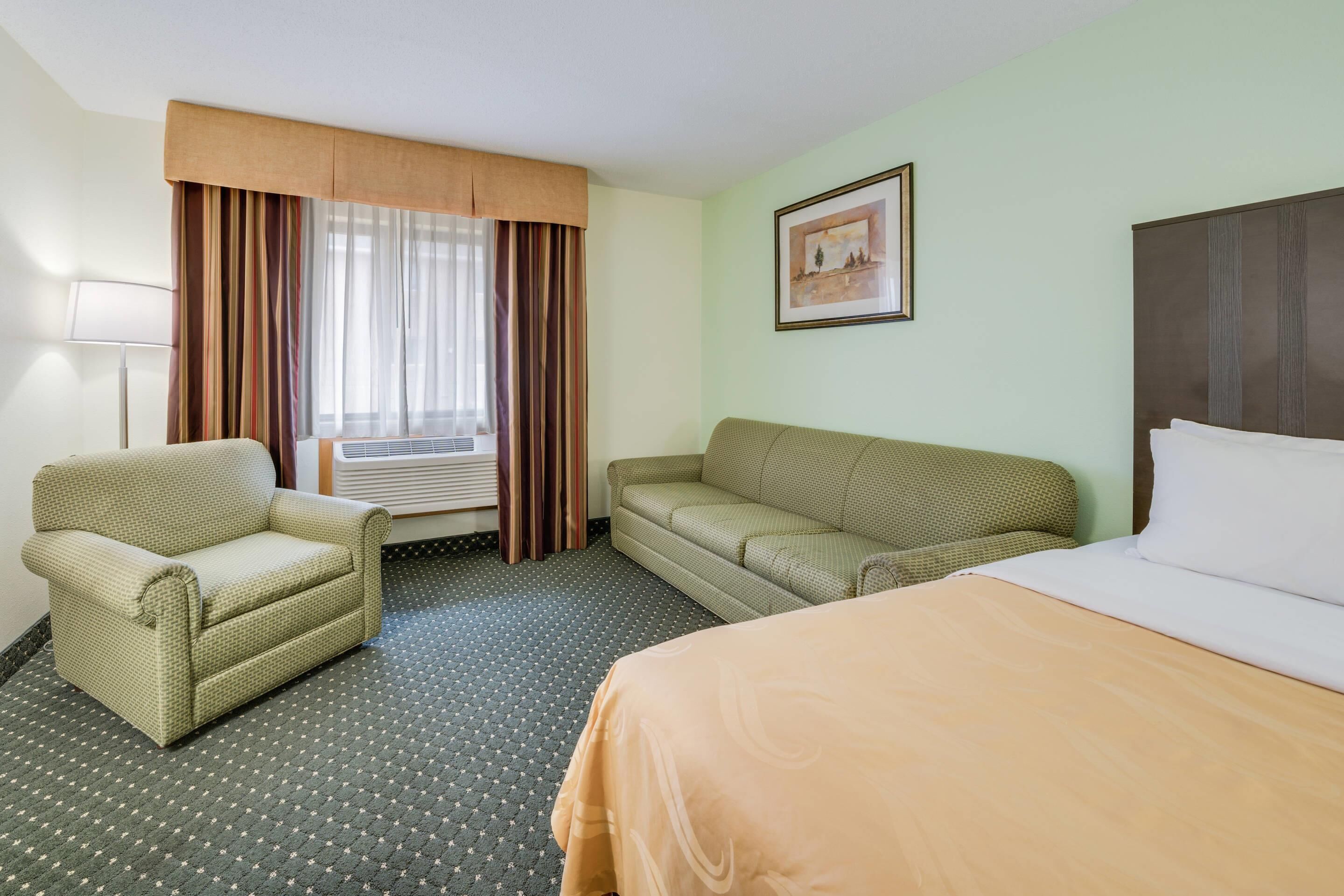 Una habitación de hotel con cama, sofá, sillón y ventana con cortinas.