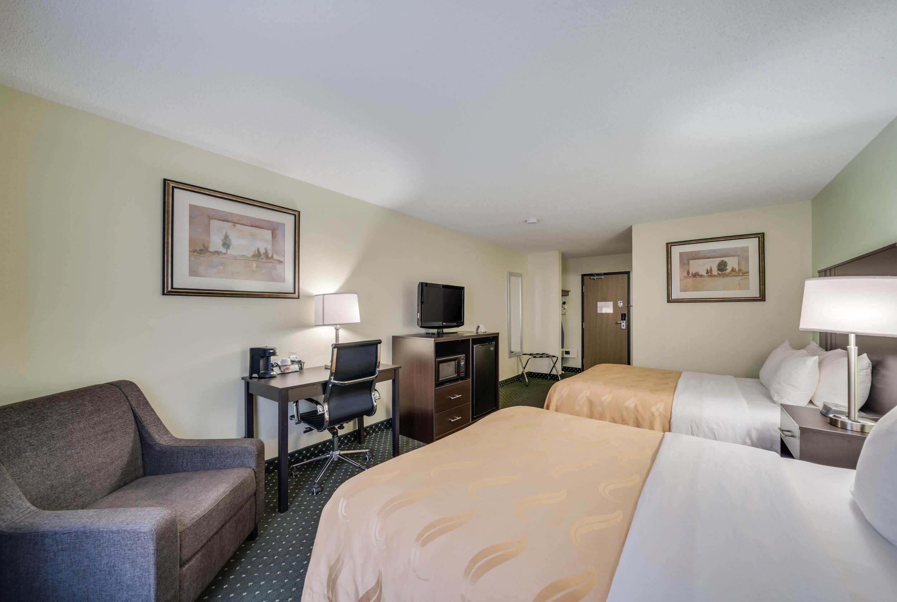 A hotel room with two beds, a desk with a computer, a TV, and a chair.