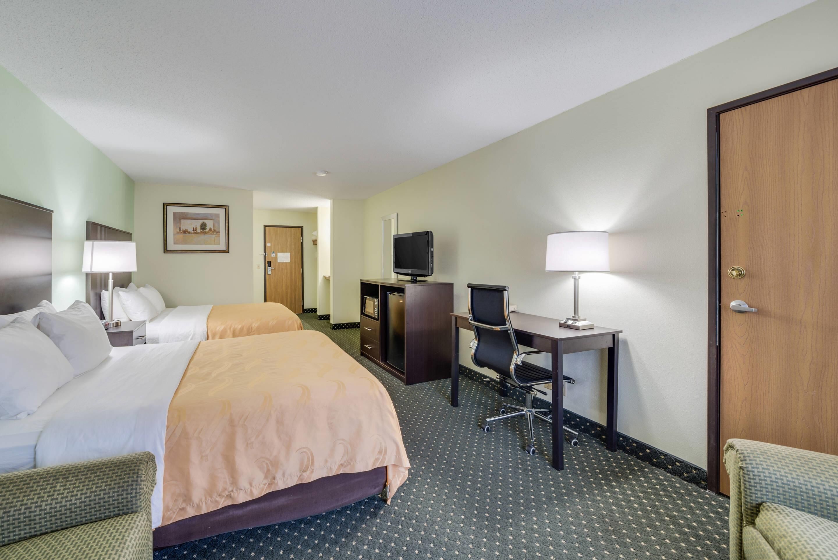 A hotel room with two beds, a desk with a chair, a television, and a door.