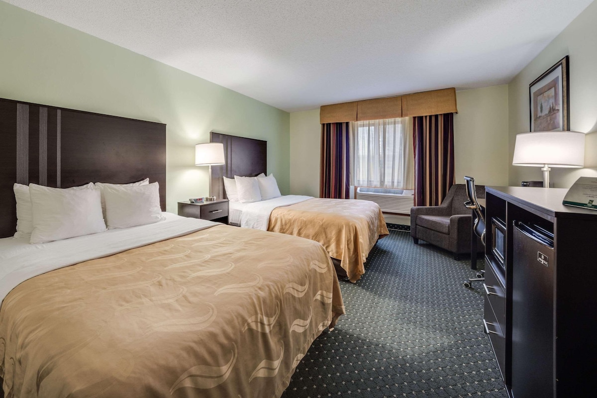 A hotel room with two beds, a desk, a chair, a dresser, and a window with curtains.