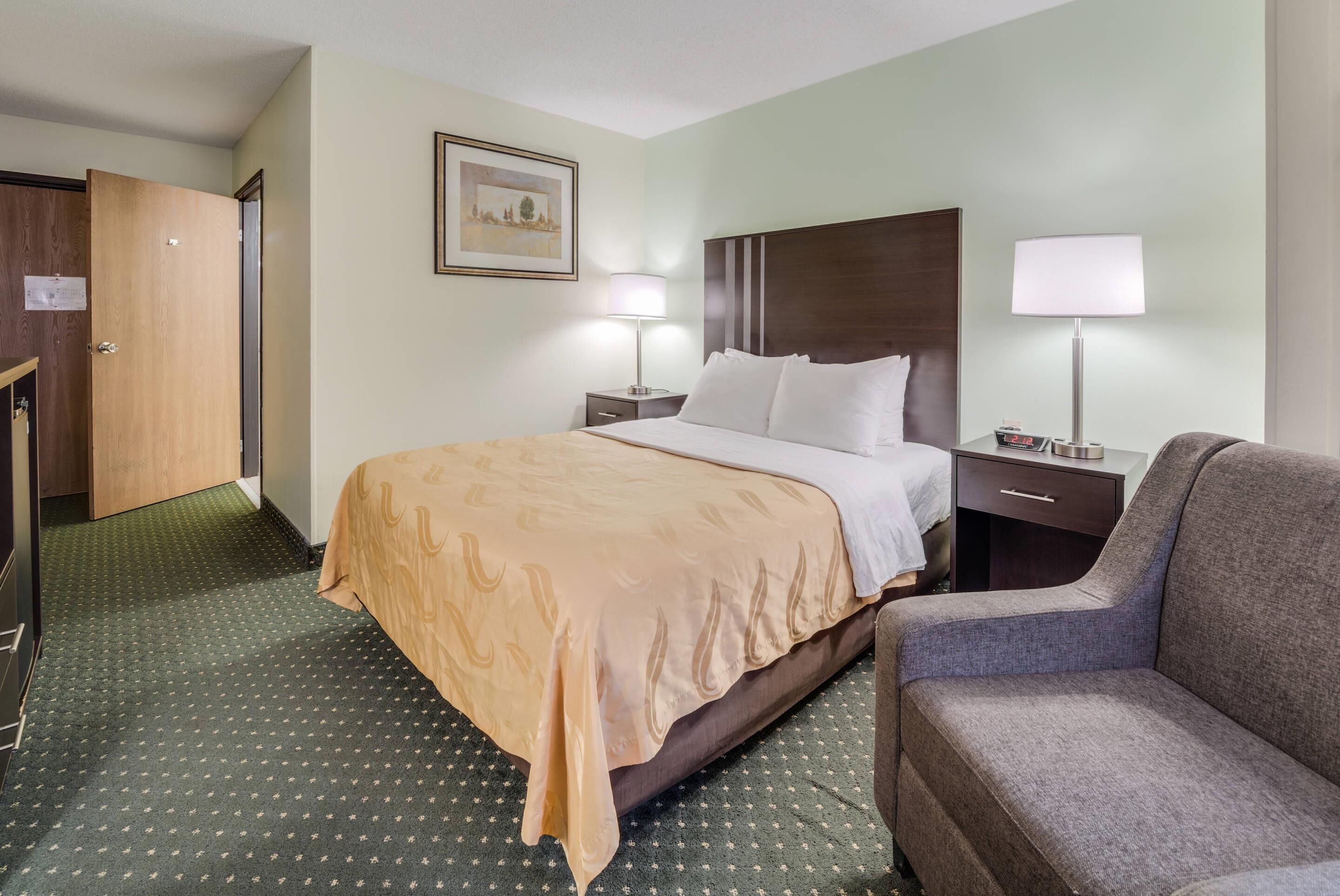 Una habitación de hotel con cama, una silla, un escritorio y una lámpara.