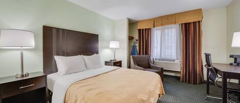 A hotel room with a large bed, a desk, a chair, a lamp, and a window with curtains.