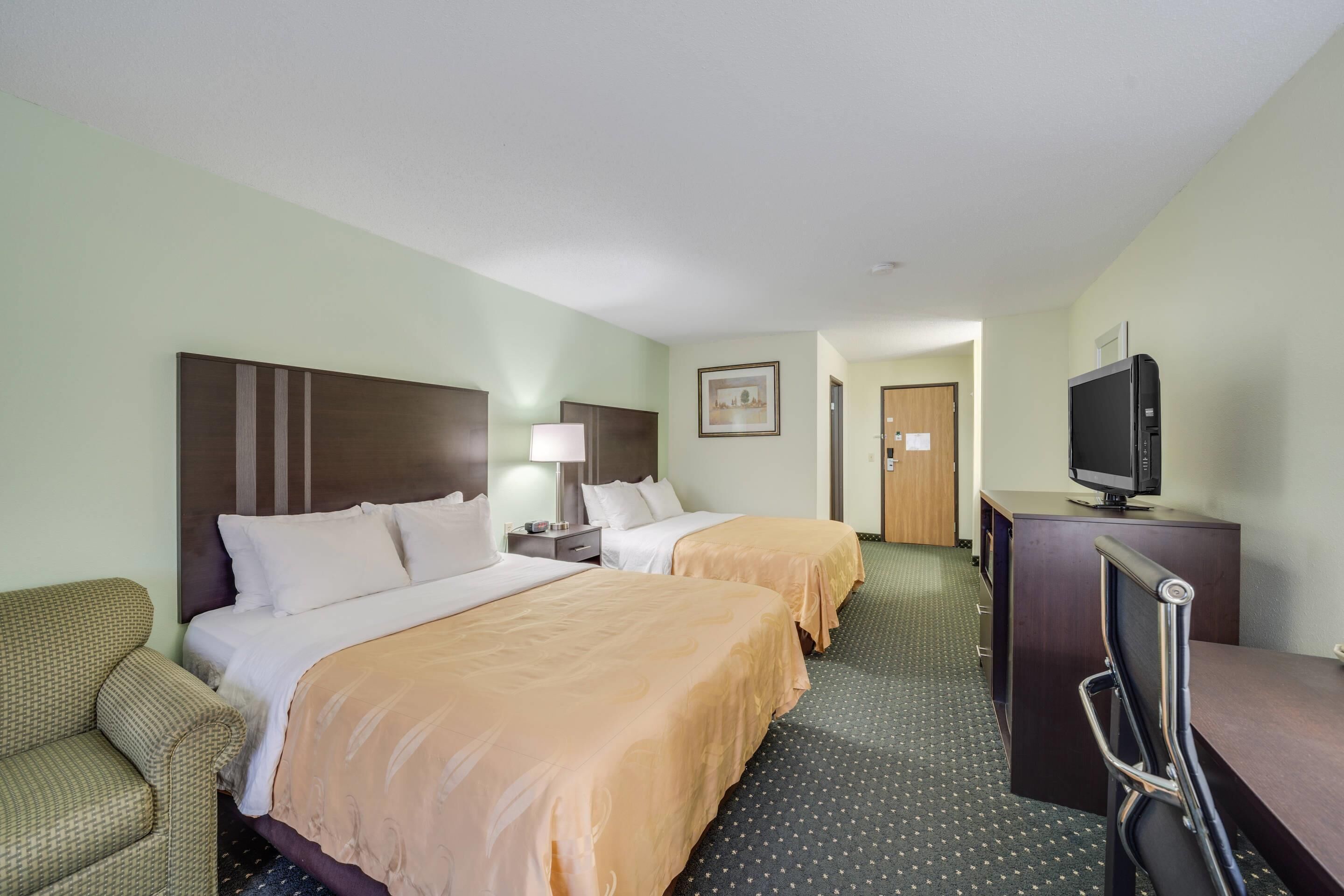 A hotel room with two beds, a desk with a television, a chair, and a small table.