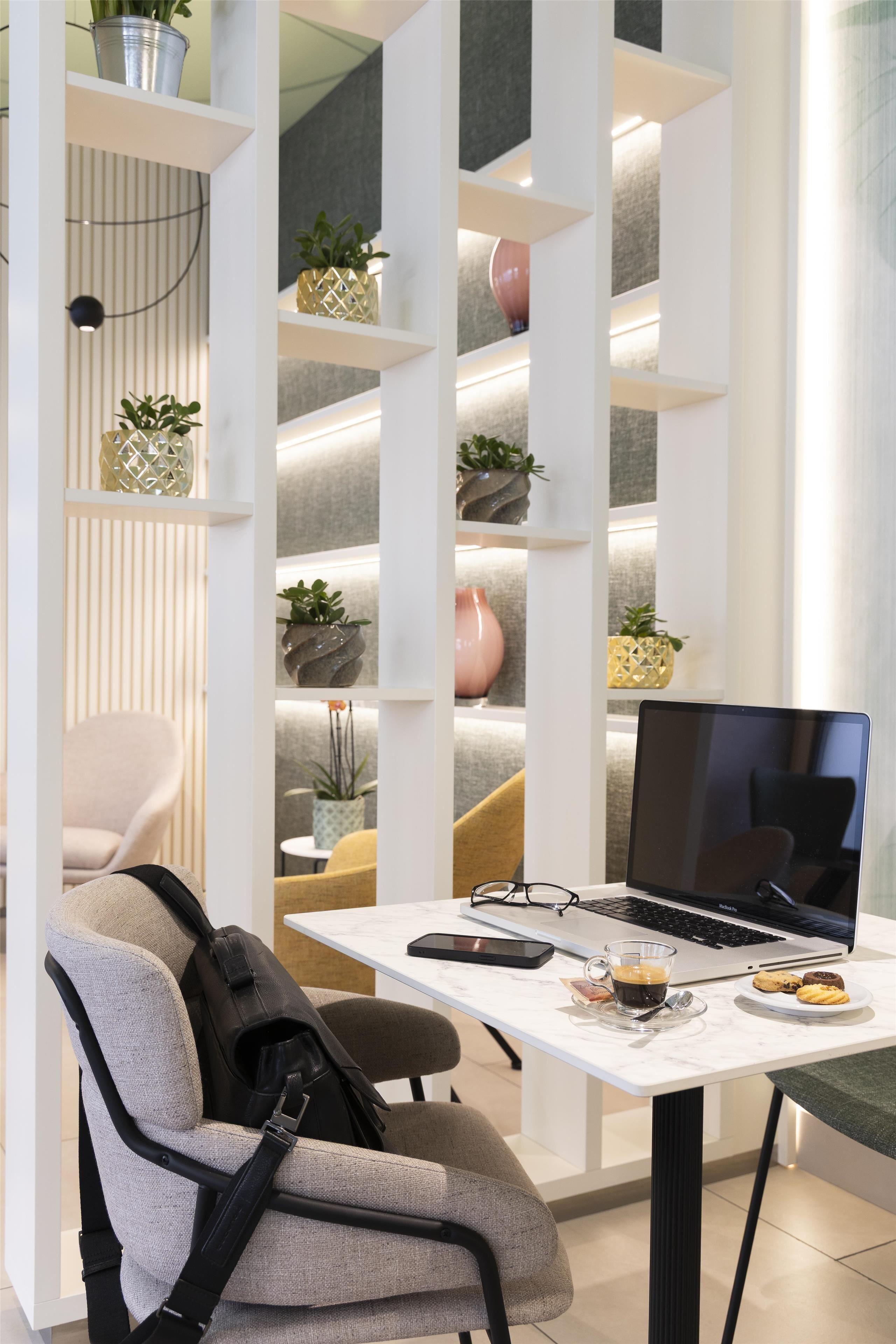 Une pièce moderne avec un bureau blanc, un ordinateur portable, une chaise et des étagères ornées de plantes.