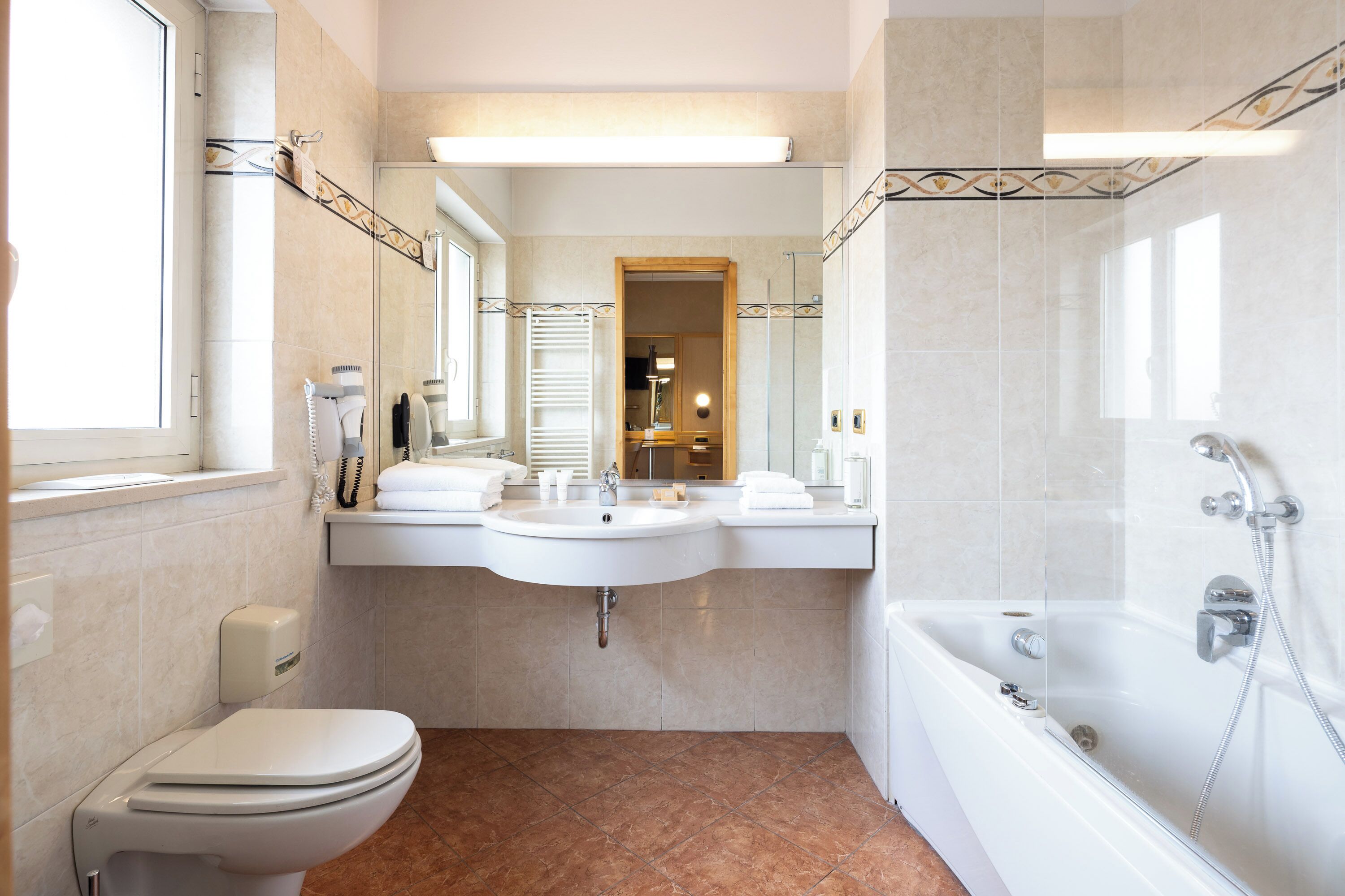 A modern bathroom with a toilet, two sinks, a mirror, and a bathtub.