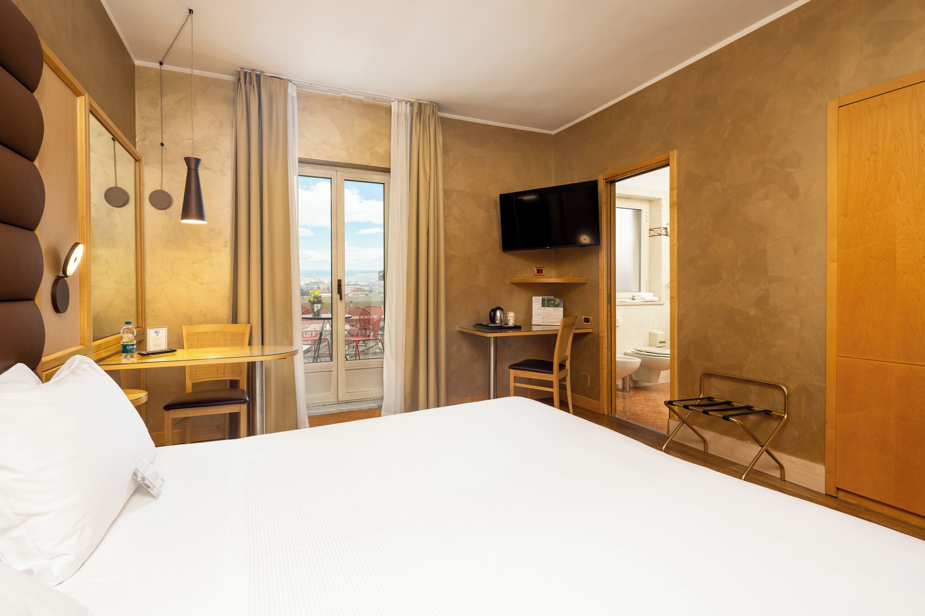 Ein Hotelzimmer mit Bett, Schreibtisch, Stuhl, Fernseher und Blick auf die Stadt.