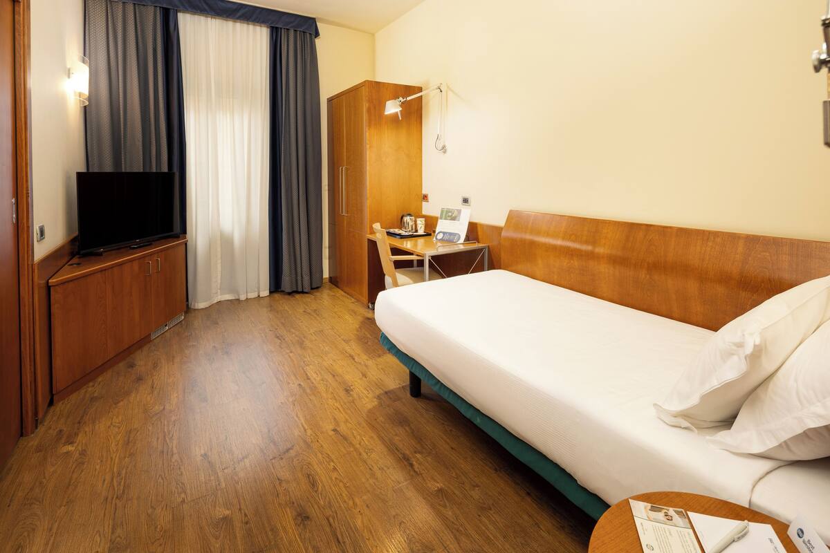 A hotel room with a bed, a desk, a television, and a wardrobe.
