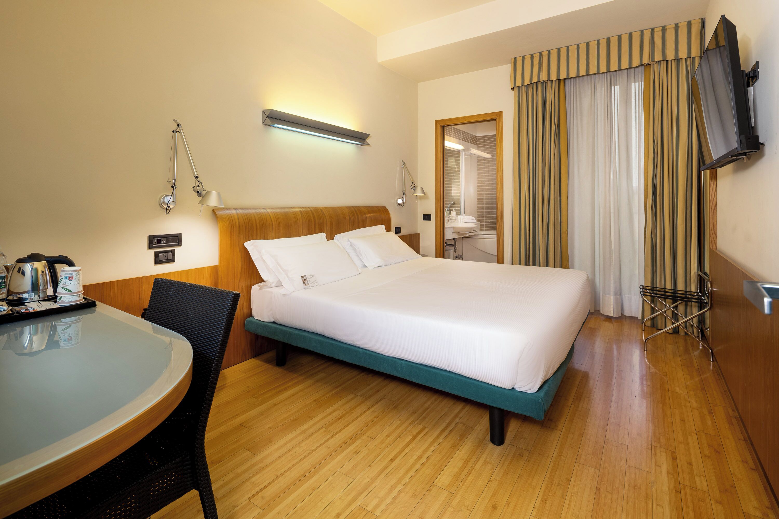 Ein Hotelzimmer mit Bett, Schreibtisch mit Stuhl, Fernseher und einem durch eine Tür sichtbaren Badezimmer.