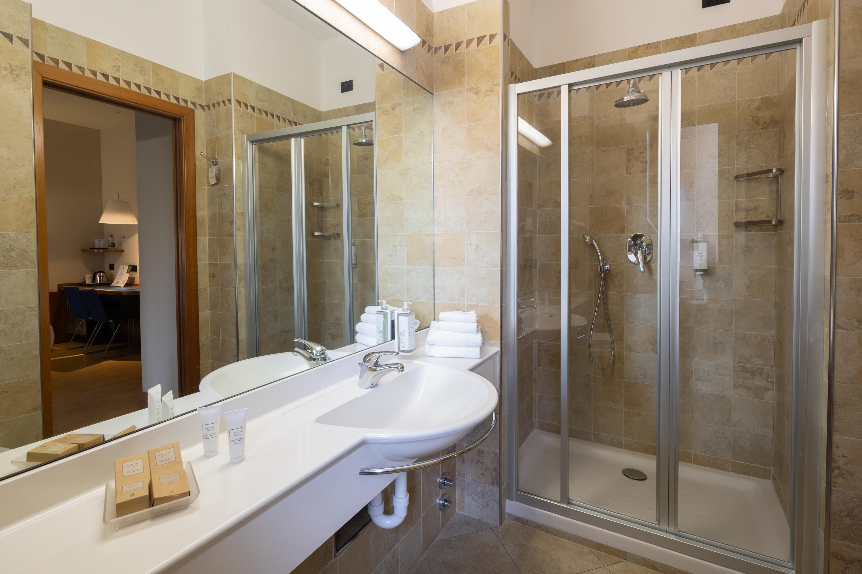 A modern bathroom with a glass-enclosed shower, a large mirror, and a white sink with toiletries.