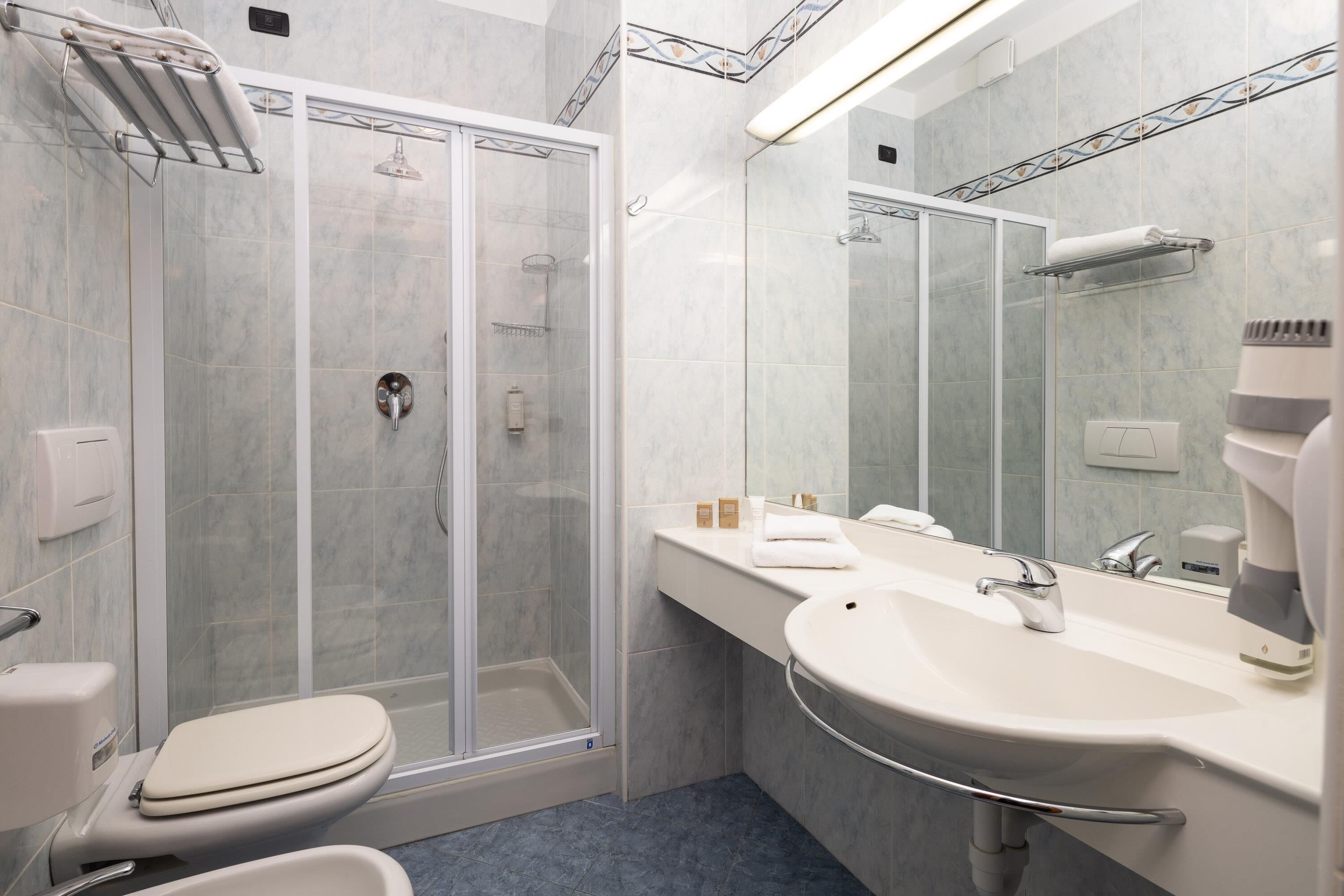 Een moderne badkamer met een douche met glazen wand, een witte wastafel en een grote spiegel.