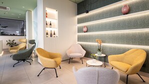 A modern interior with a reception desk, seating area with armchairs, a small table with a vase, and a wall with shelves. - Best Western Hotel Luxor (Turin)