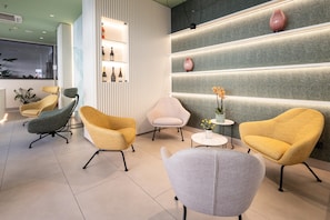 A modern interior with a reception desk, seating area with armchairs, a small table with a vase, and a wall with shelves. - Best Western Hotel Luxor (Turin)