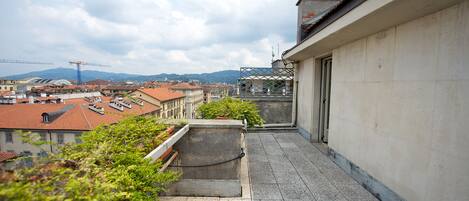 A narrow balcony with a view of a cityscape, including buildings and a distant mountain range.