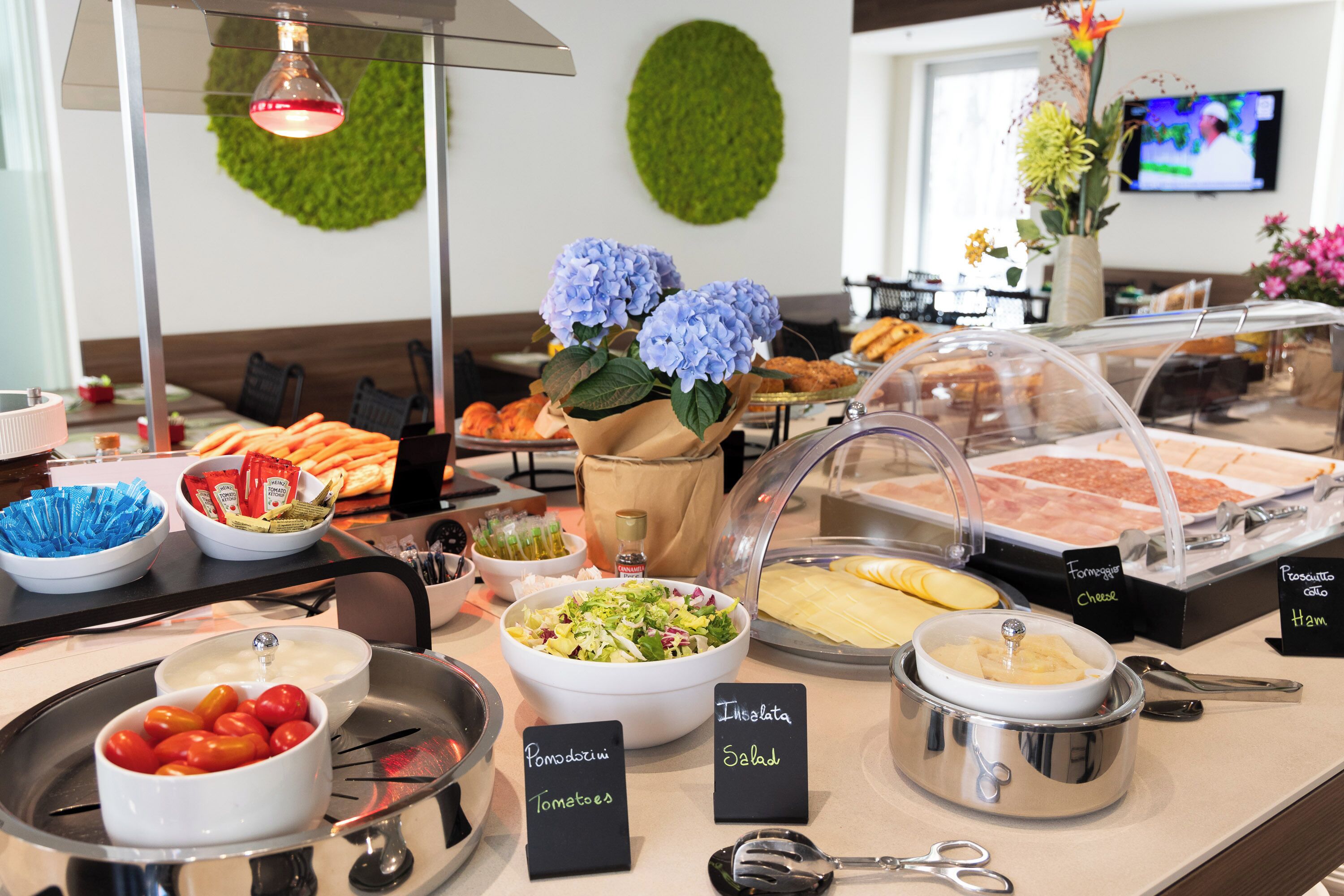 A buffet with various food options, including a bowl of tomatoes, a salad, and a container of cheese.