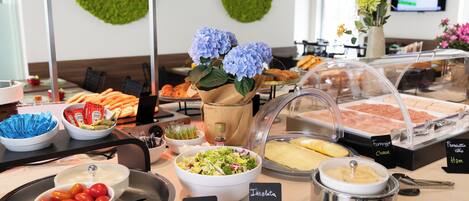 A buffet with various food options, including a bowl of tomatoes, a salad, and a container of cheese.