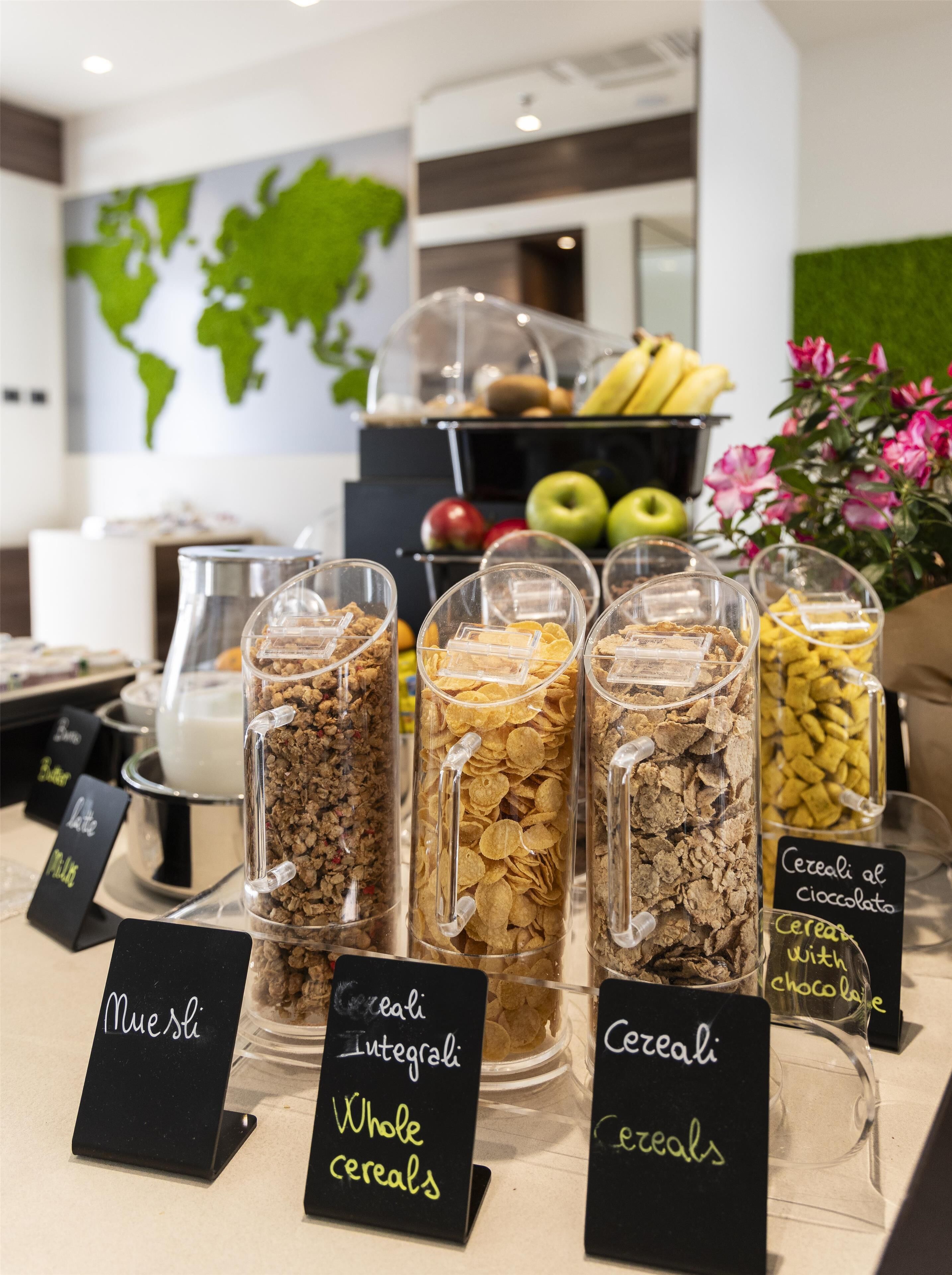 A breakfast buffet with labeled containers of whole cereals, including muesli, integral, and cereal with chocolate.