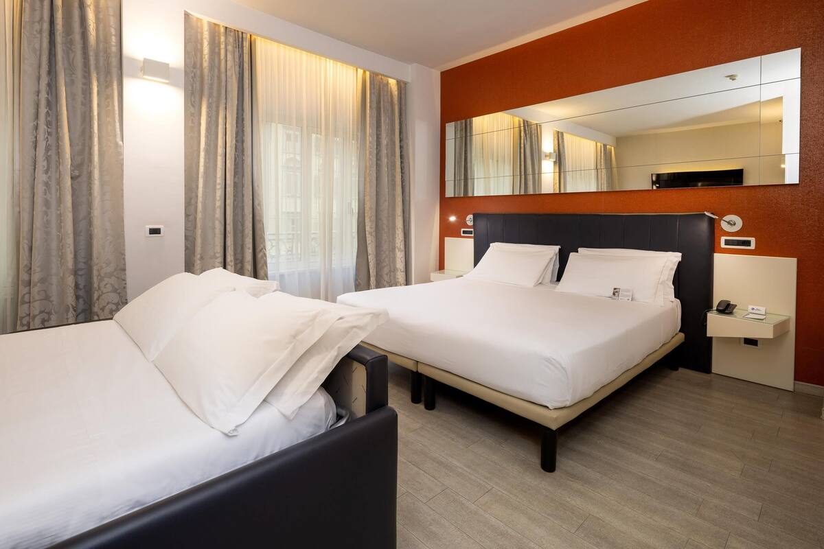 A hotel room with two beds, a large mirror, and a bedside table with a phone.