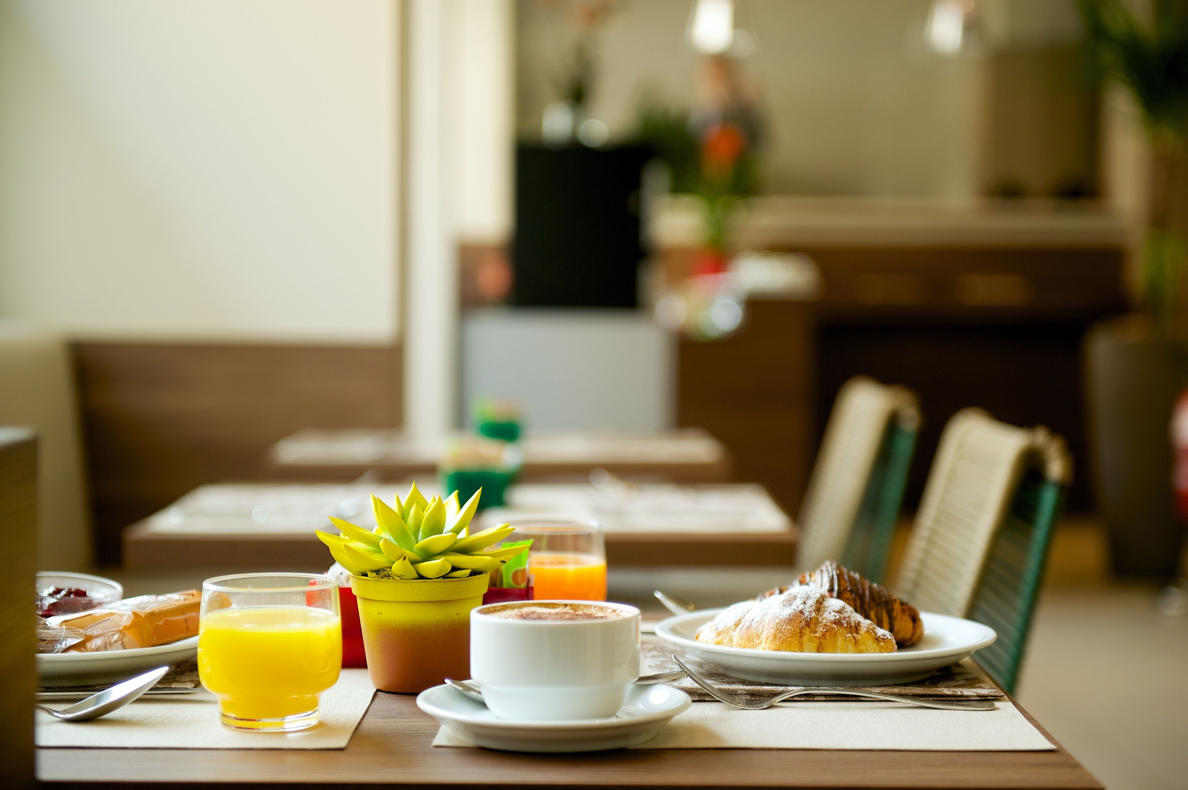Desayuno con una bandeja de pasteles, un vaso de zumo de naranja, una taza de café y una pequeña planta en maceta.