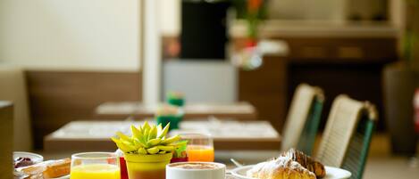 Ein Frühstückstisch mit Gebäck, Orangensaft, Kaffee und einem kleinen Blumentopf.