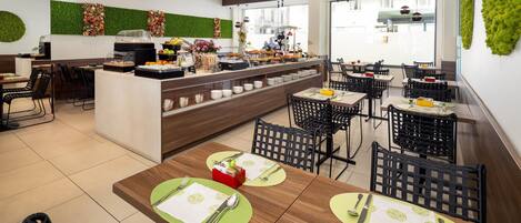 A modern restaurant with a buffet area, multiple dining tables with green placemats, and a green wall with a vertical garden.