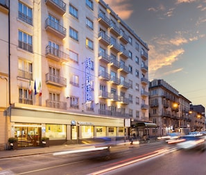 A multi-story hotel with balconies, a visible entrance, and a street view with moving traffic.