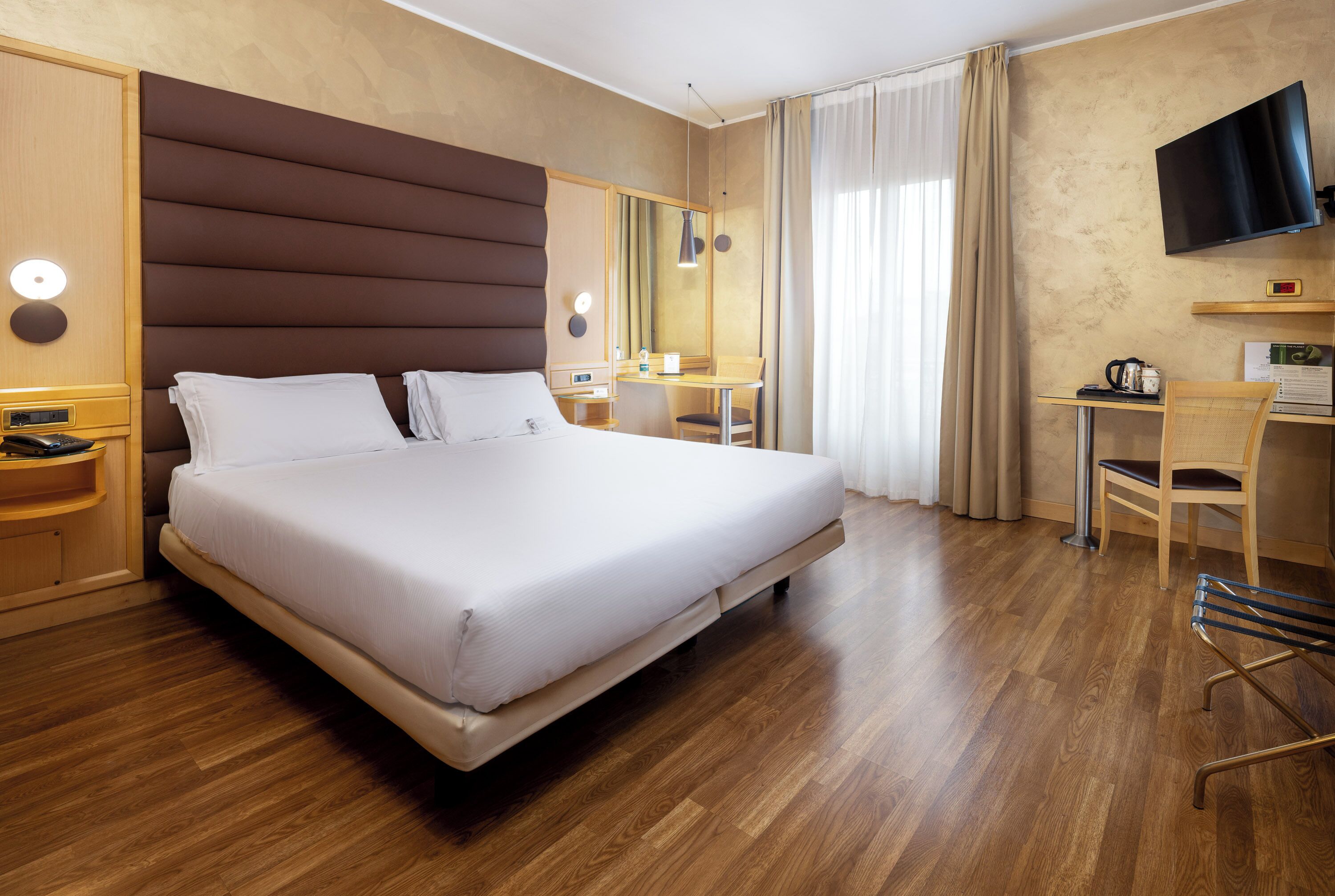 Habitació d'hotel amb un llit gran, un escriptori amb cadira, un televisor i un mirall.