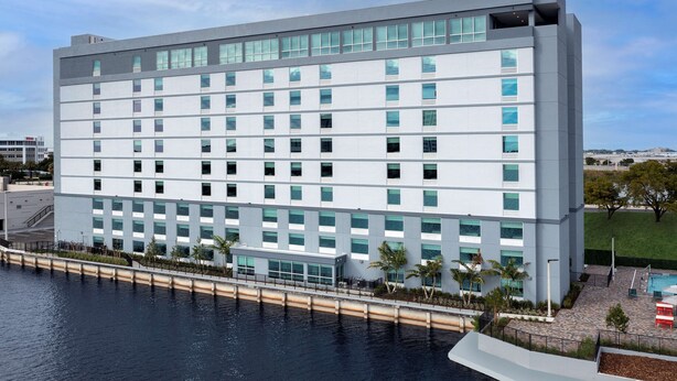 A modern hotel with a white facade, multiple floors, and a pool area with palm trees. - TRU by Hilton Miami Airport South Blue Lagoon, FL (Miami)