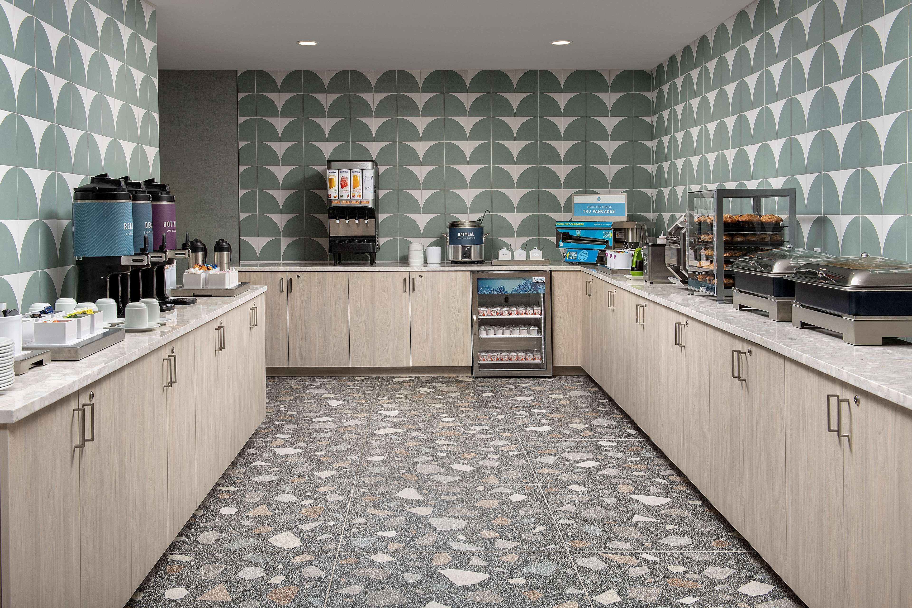 A modern kitchen with a geometric tile backsplash, a coffee machine, and a refrigerated display case.