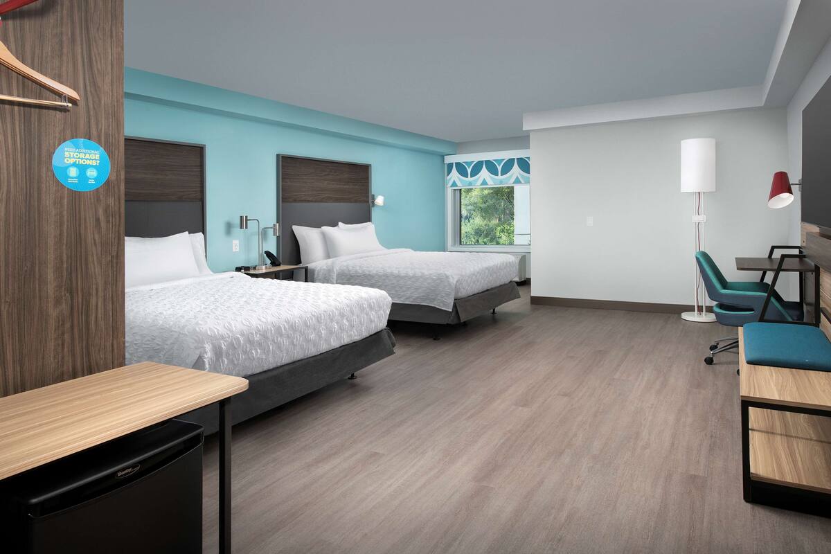 Una habitación de hotel moderna con dos camas, un escritorio, una silla y vistas a zonas verdes.