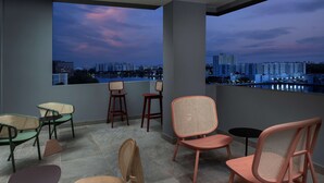 A balcony with a city view, featuring a mix of wooden and wicker chairs, a small round table, and a view of a river and buildings. - TRU by Hilton Miami Airport South Blue Lagoon, FL (Miami)