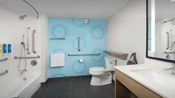 Une salle de bain moderne équipée d’une baignoire, de toilettes et d’un lavabo, avec un mur bleu orné de motifs circulaires et un miroir au-dessus du lavabo.