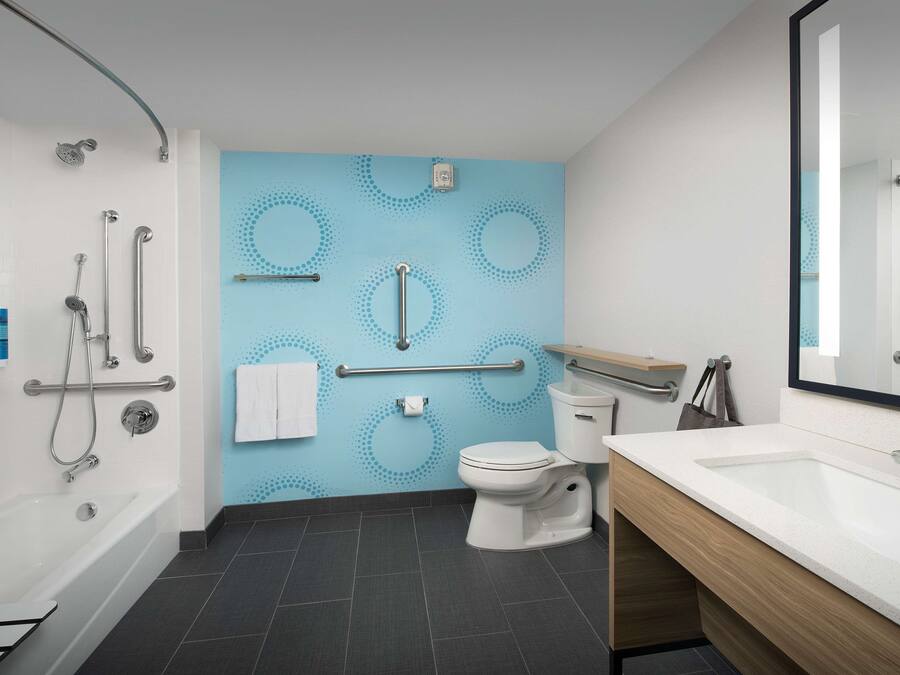 Une salle de bain moderne équipée d’une baignoire, de toilettes et d’un lavabo, avec un mur bleu orné de motifs circulaires et un miroir au-dessus du lavabo.