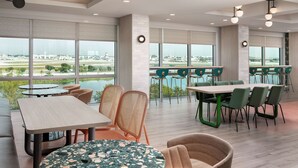 A modern hotel lobby with large windows, multiple seating areas, and a view of the airport. - TRU by Hilton Miami Airport South Blue Lagoon, FL (Miami)