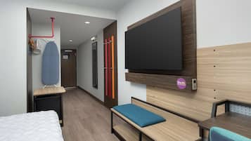 Quarto de hotel moderno com cama, escrivaninha, um banco, televisão e área de chuveiro.