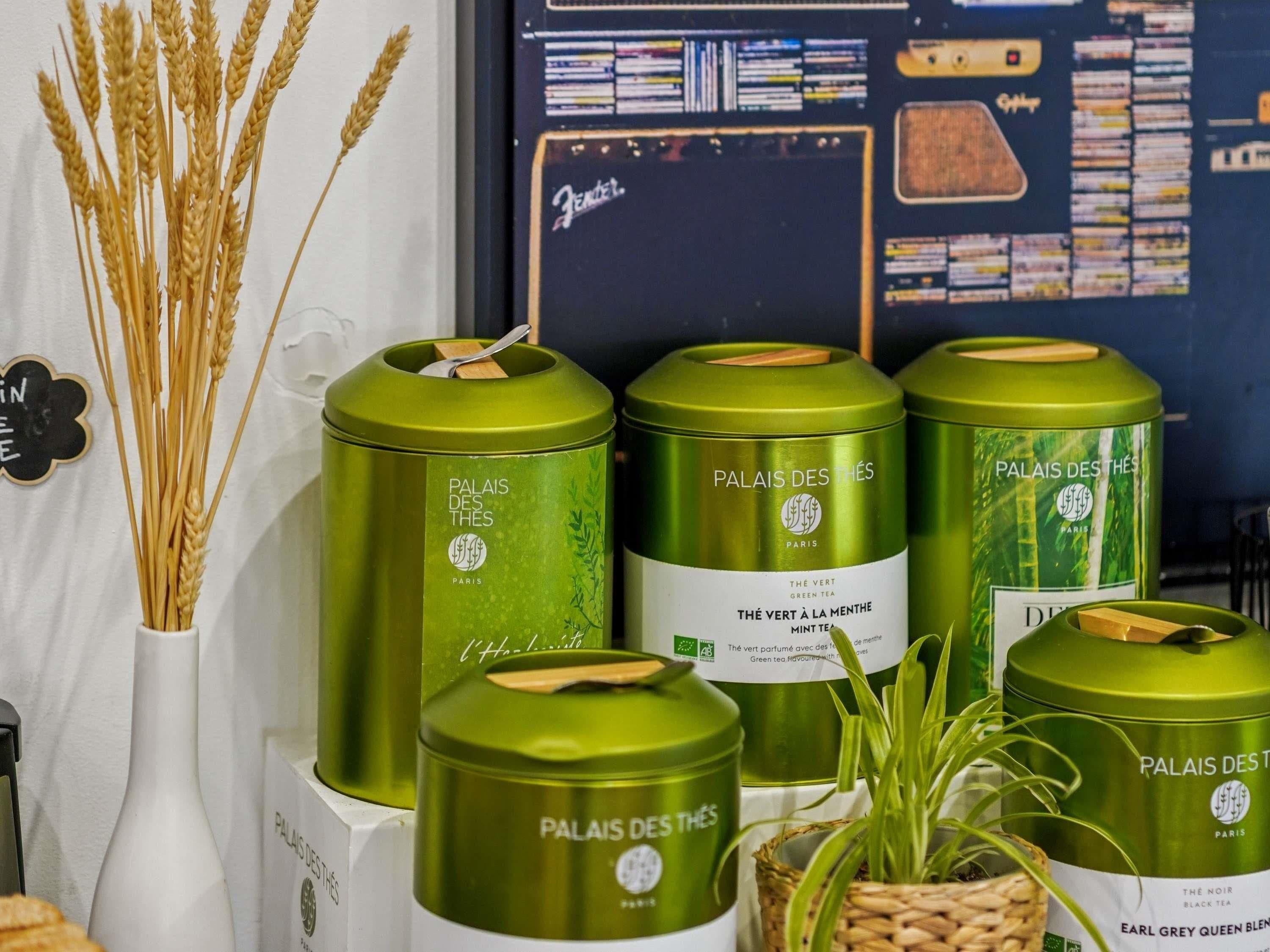 A display of green tea tins labeled 'Palais des Thés' with a white vase containing wheat stalks.