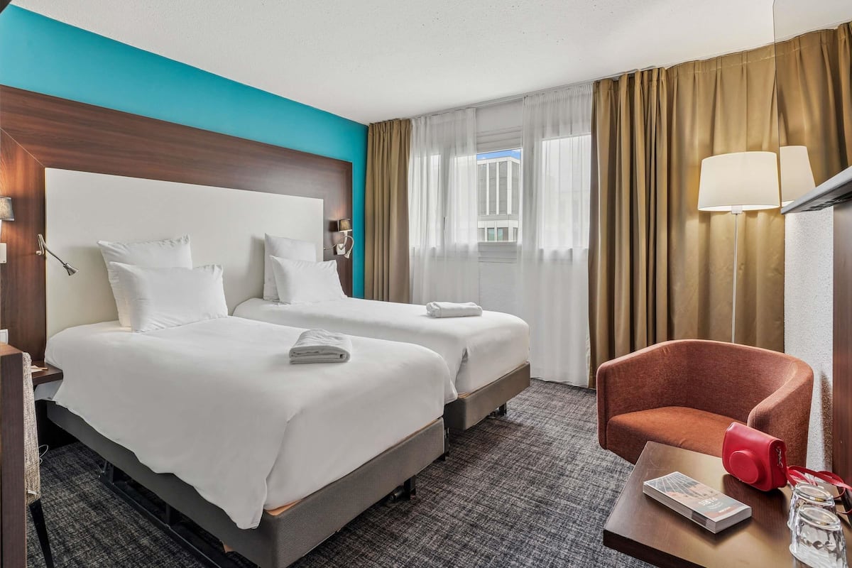 Ein Hotelzimmer mit zwei Betten, einem Schreibtisch, einem Stuhl und einer Lampe.