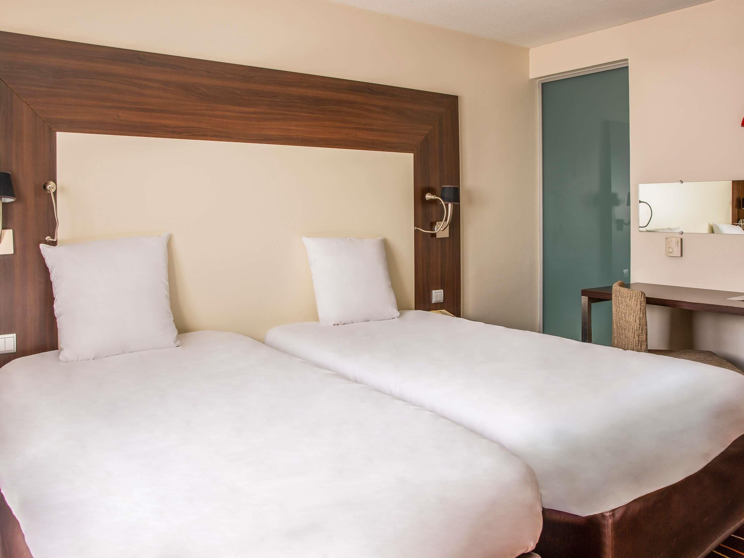 A hotel room with two beds, a wooden headboard, a desk, and a mirror.