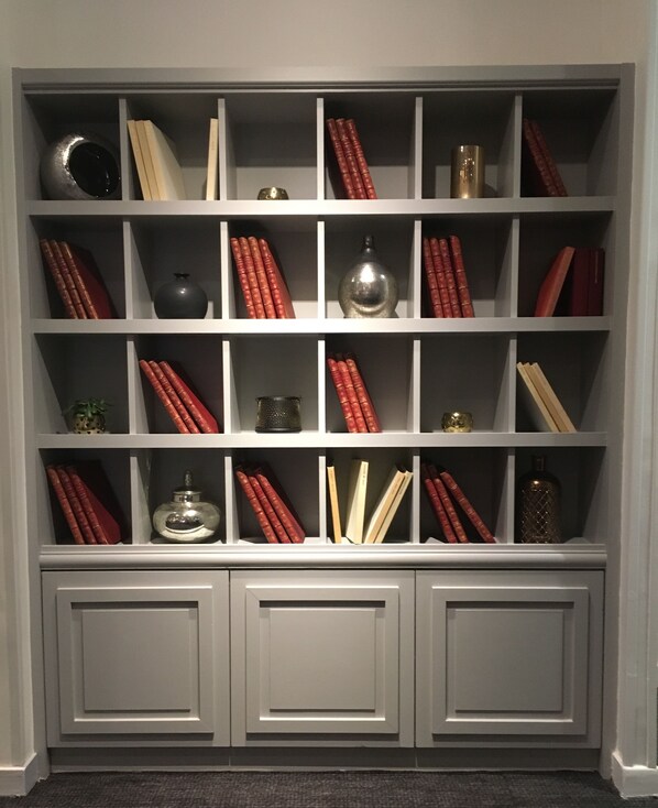 A bookshelf with multiple shelves, each containing books and decorative items. - Mercure Paris Porte d'Orléans (Montrouge)