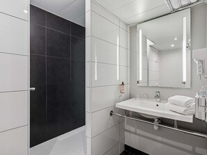 Un baño moderno con cabina de ducha negra, azulejos blancos, un espejo grande y un lavamanos blanco con toallero.