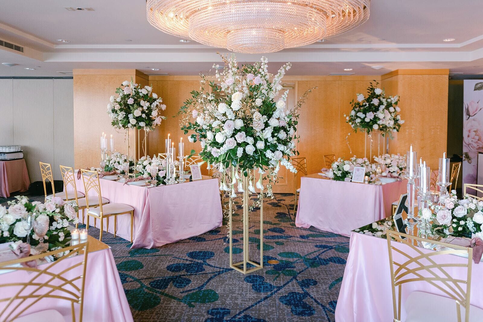 A banquet hall with round tables, floral centerpieces, and a chandelier.