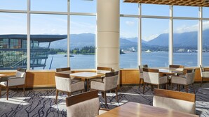 A modern dining area with large windows offering a view of a lake and mountains. - Pan Pacific Vancouver (Vancouver)