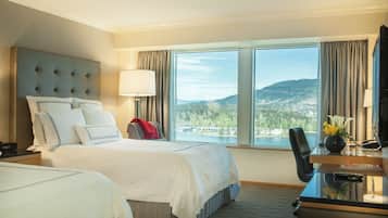 Habitación de hotel con una cama grande, un escritorio, una silla y vistas a un lago y montañas.