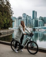 Una persona pedaleando en una bicicleta estática cerca de un frente marítimo, con un horizonte urbano al fondo.