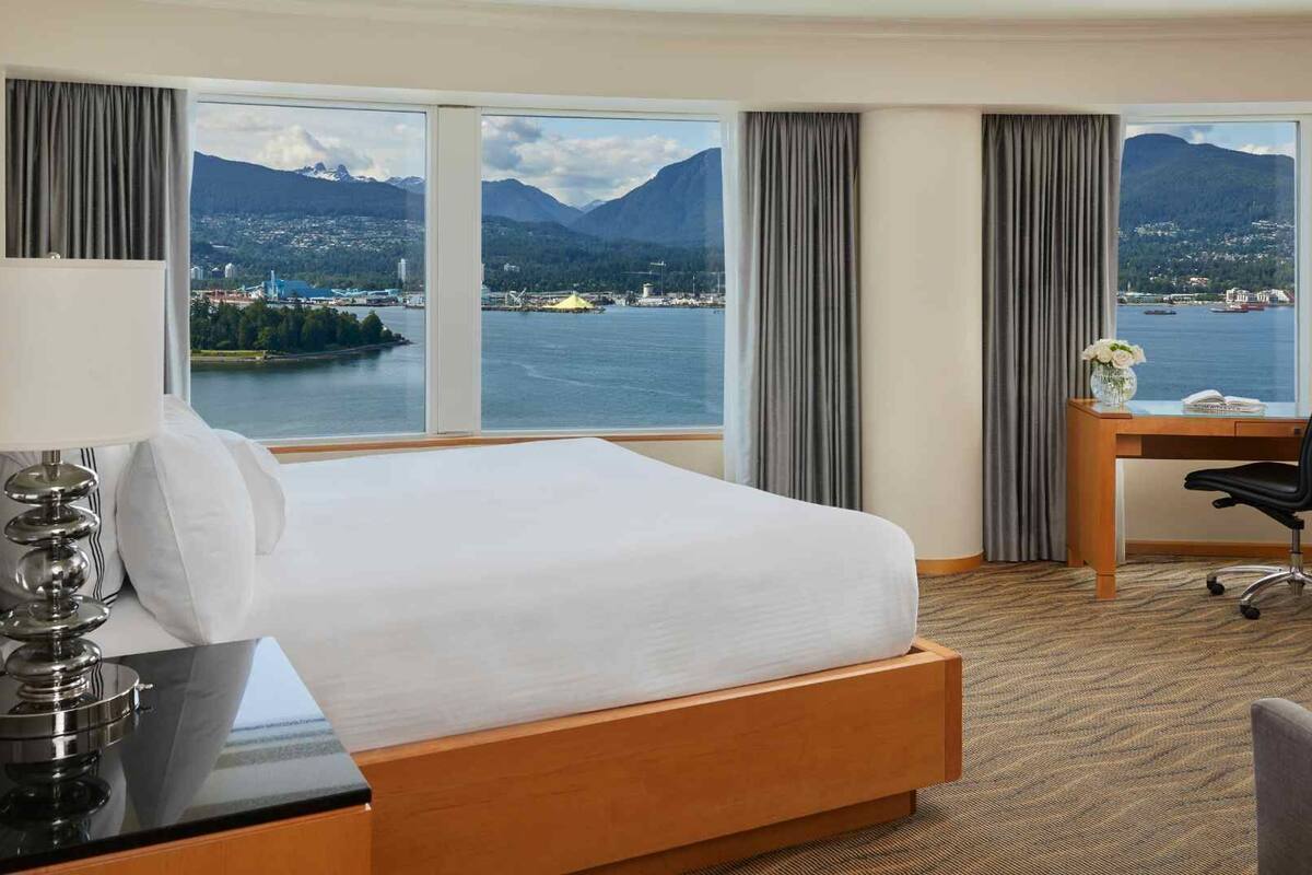 A hotel room with a large bed, a desk, and a chair. The room has a view of a lake and mountains.