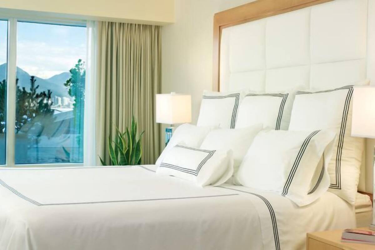 A hotel room with a large bed, a window with a view of mountains, and a nightstand with a lamp.