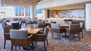 A spacious dining area with multiple tables and chairs, a marble wall, and large windows offering a view.