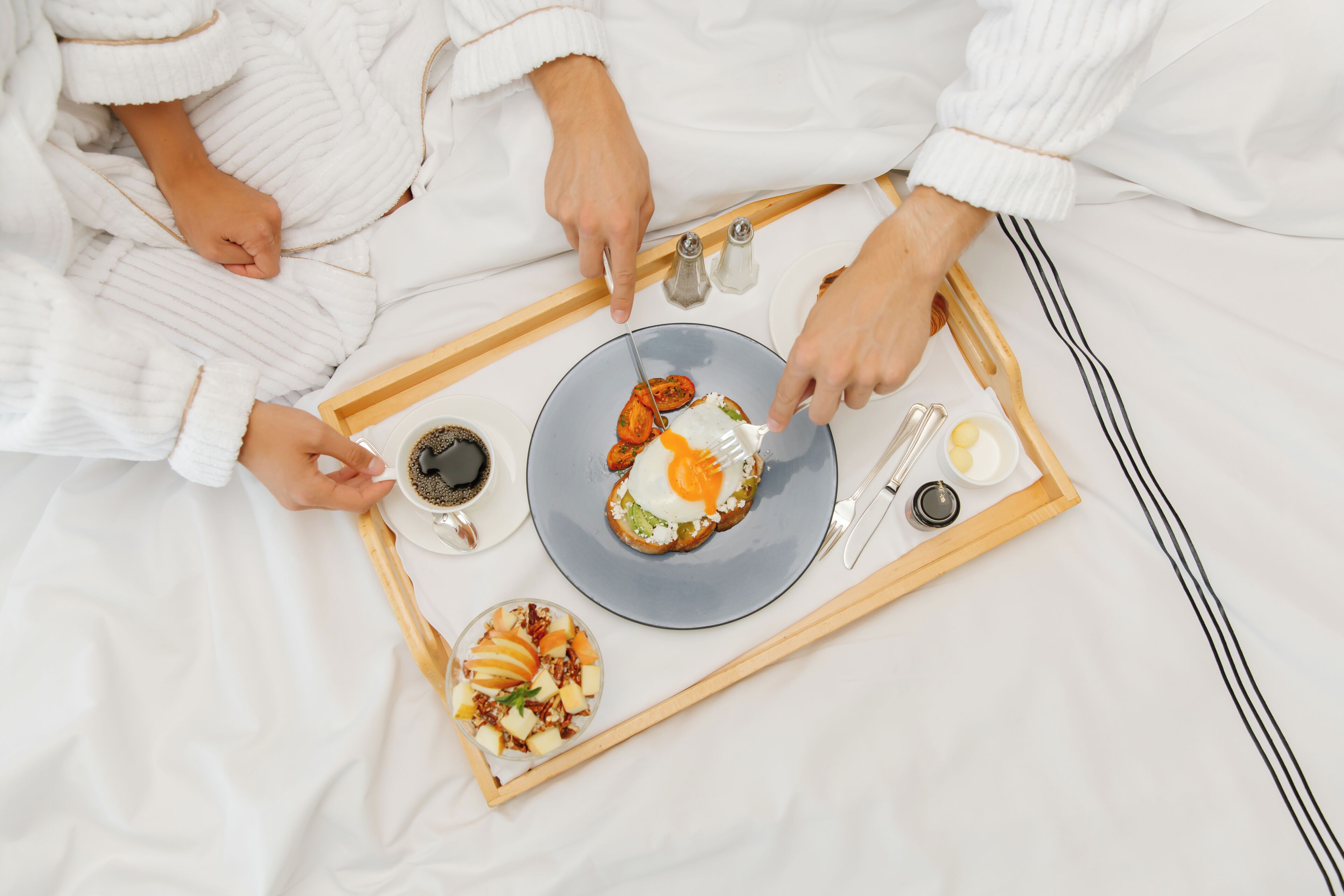 A breakfast tray with a plate of food, a cup of coffee, and condiments on a bed.