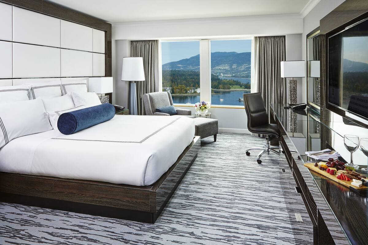 A modern hotel room with a large bed, a desk, a chair, and a TV.